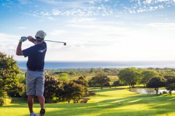 Image d'un golfeur jouant sur un parcours de golf de l'île Maurice, offrant une vue imprenable sur l'océan Indien et les montagnes environnantes